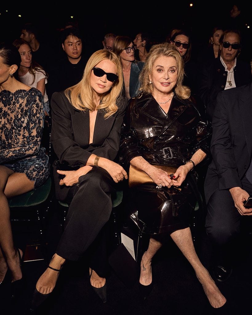 Virginie Efira in black Saint Laurent tailoring alongside Catherine Deneuve in a glossy Saint Laurent trench coat in Paris.